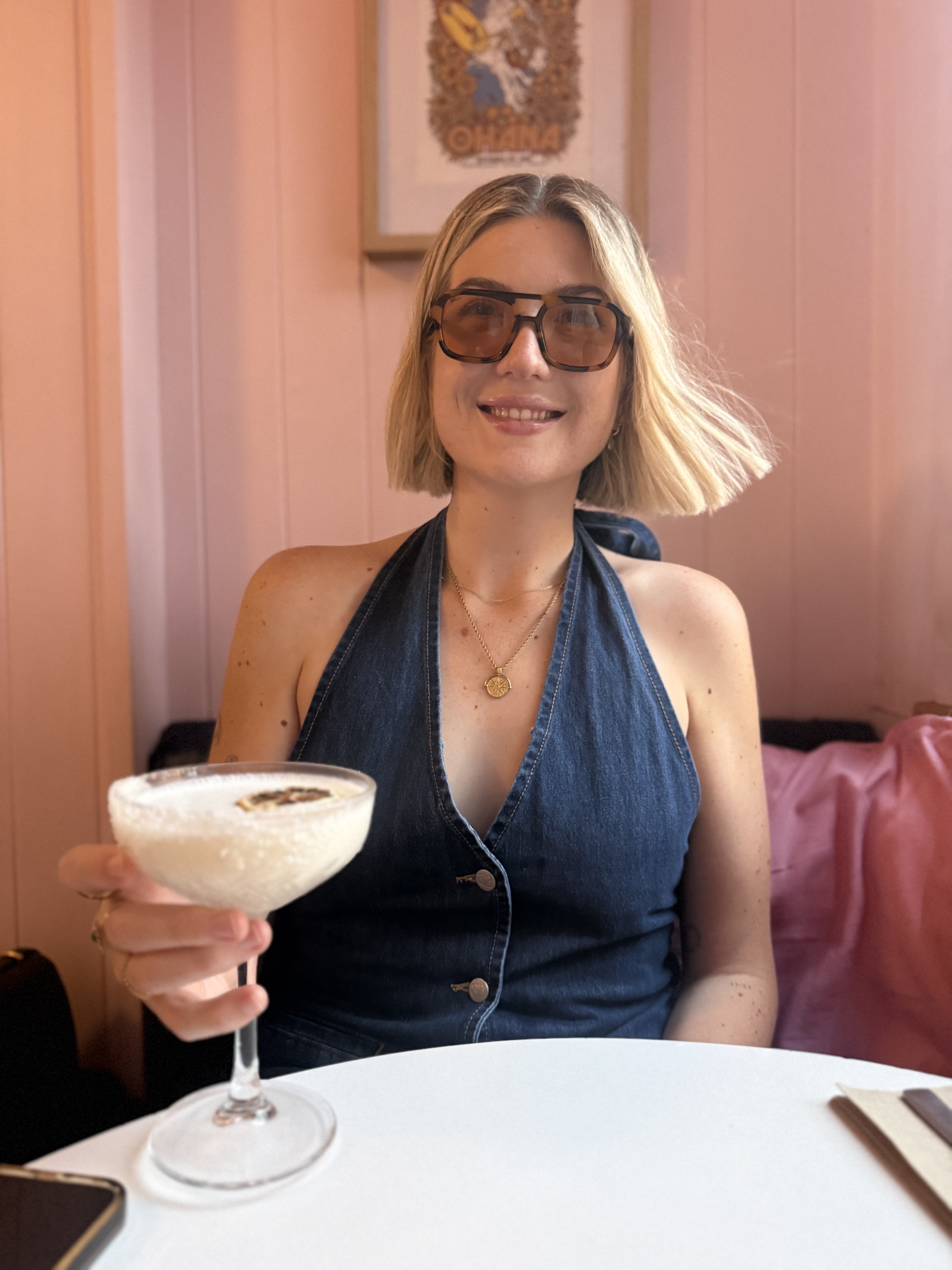 Mikaila in sunglasses, smiling with a cocktail, ready to pick something to eat